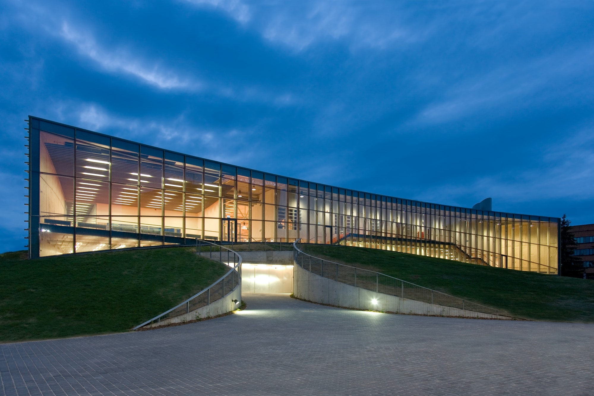 Modern university buildings, glass facade lit up at night, on a curved ground surface